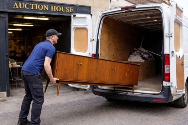 A driver loading a large piece of auction furniture into a delivery van